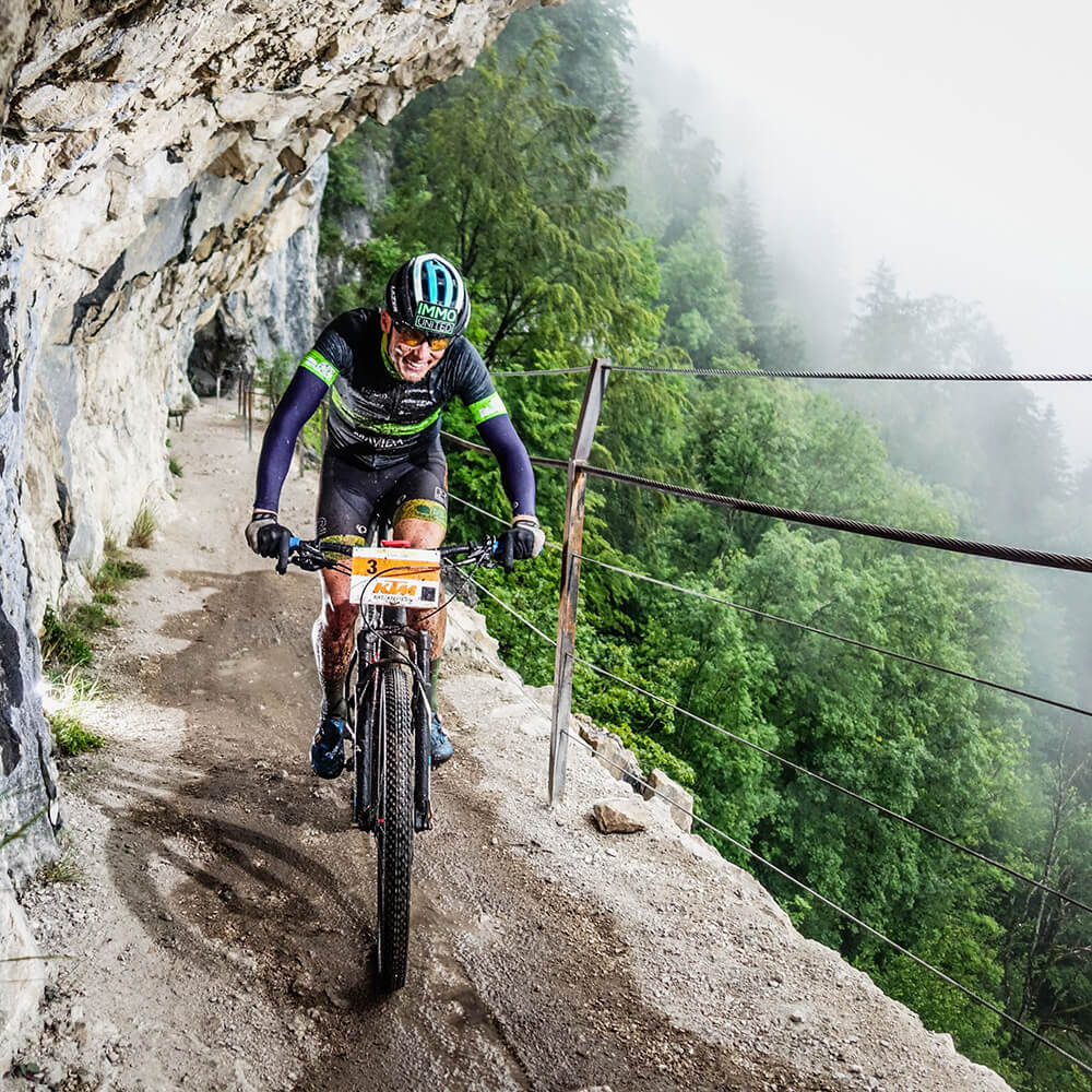 Sponsoring_Sportsponsoring_Lukas Kaufmann03_Lukas Kaufmann Lukas Kaufmann auf dem Rad auf einem schmalen Bergweg an einer Felswand - Copyright Sportograf.com